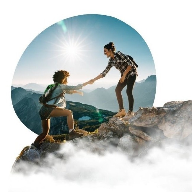 Two women helping each other hike up a mountain